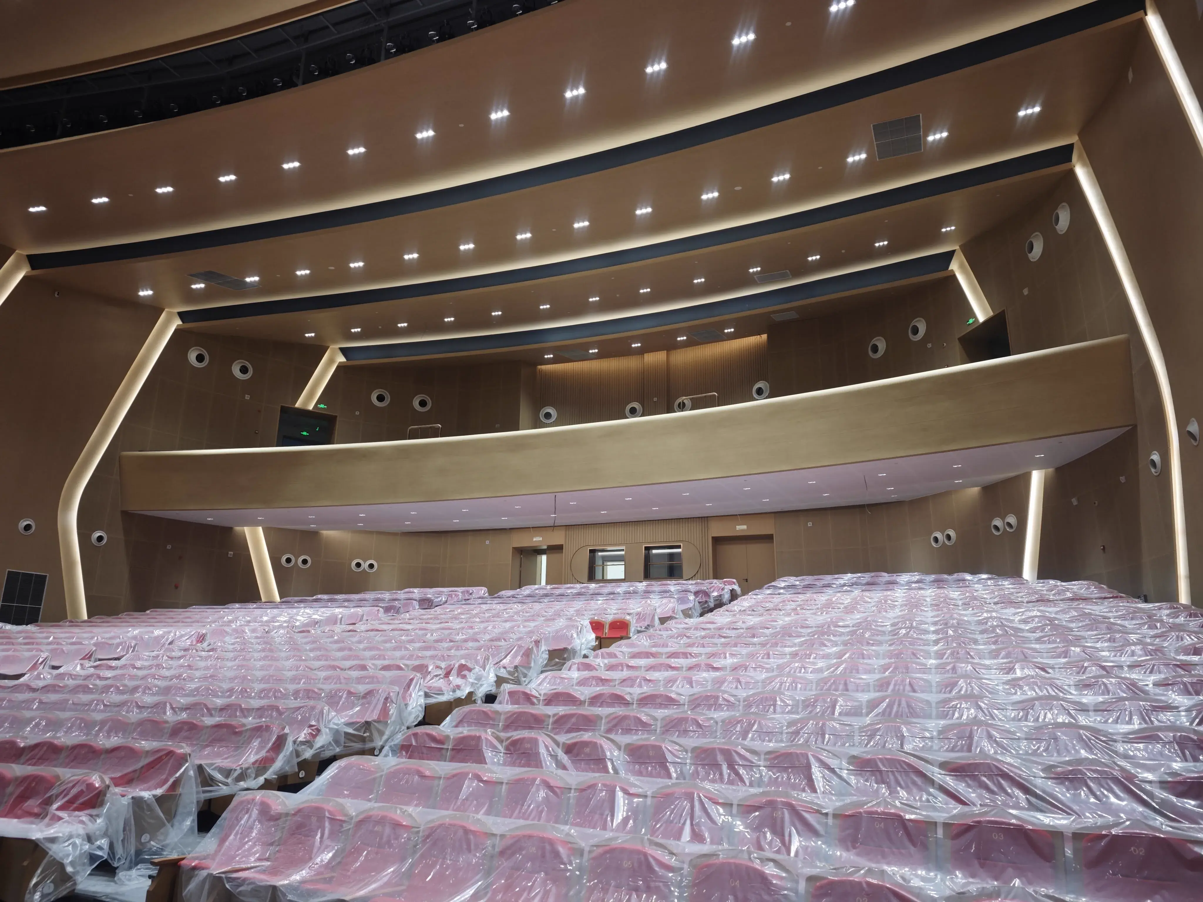 多功能礼堂座席区,包含红色织物座椅、楼座与暖木色声学饰面