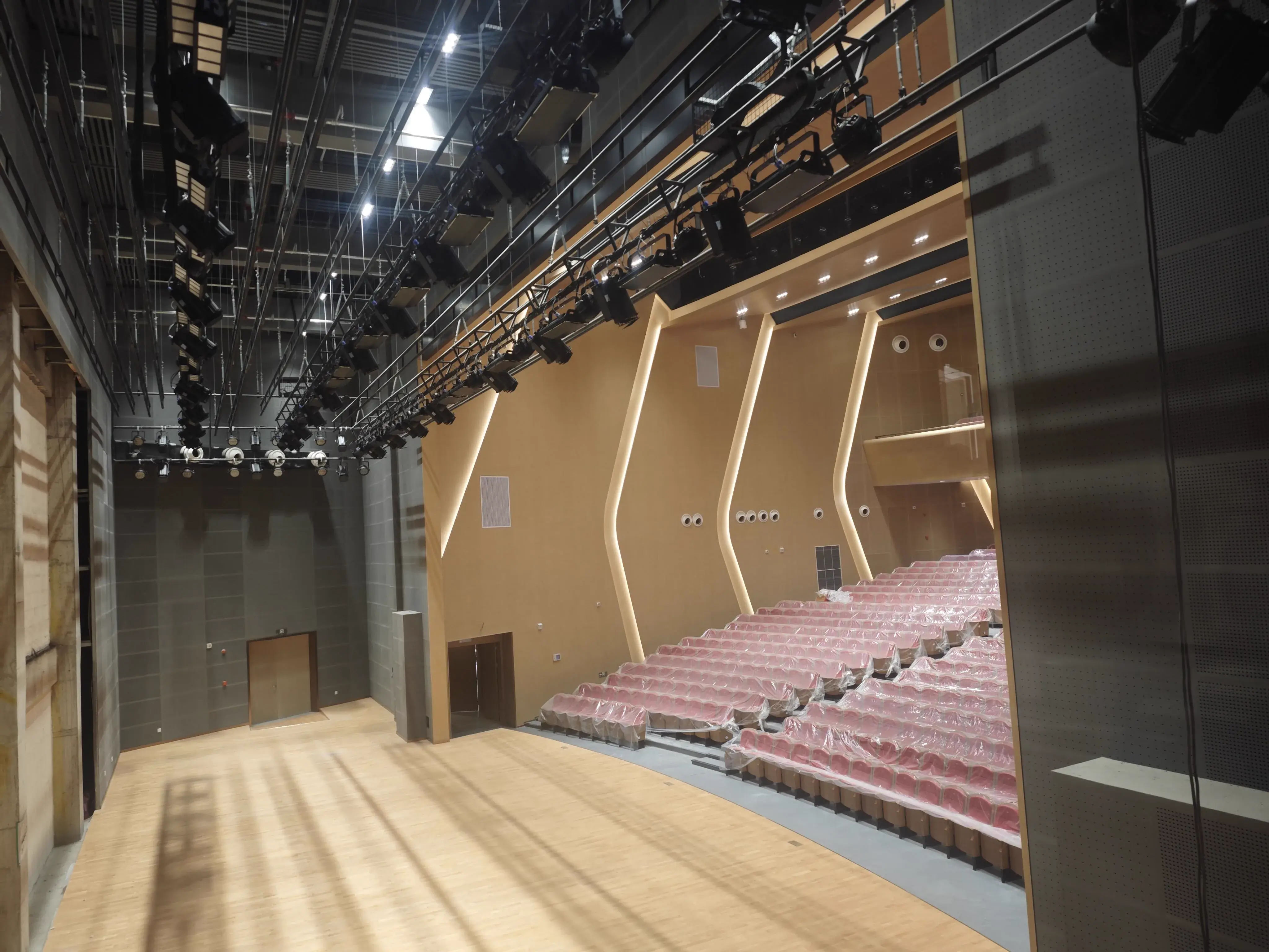 Panoramic auditorium view from the stage side with proscenium, lighting trusses, and tiered seating