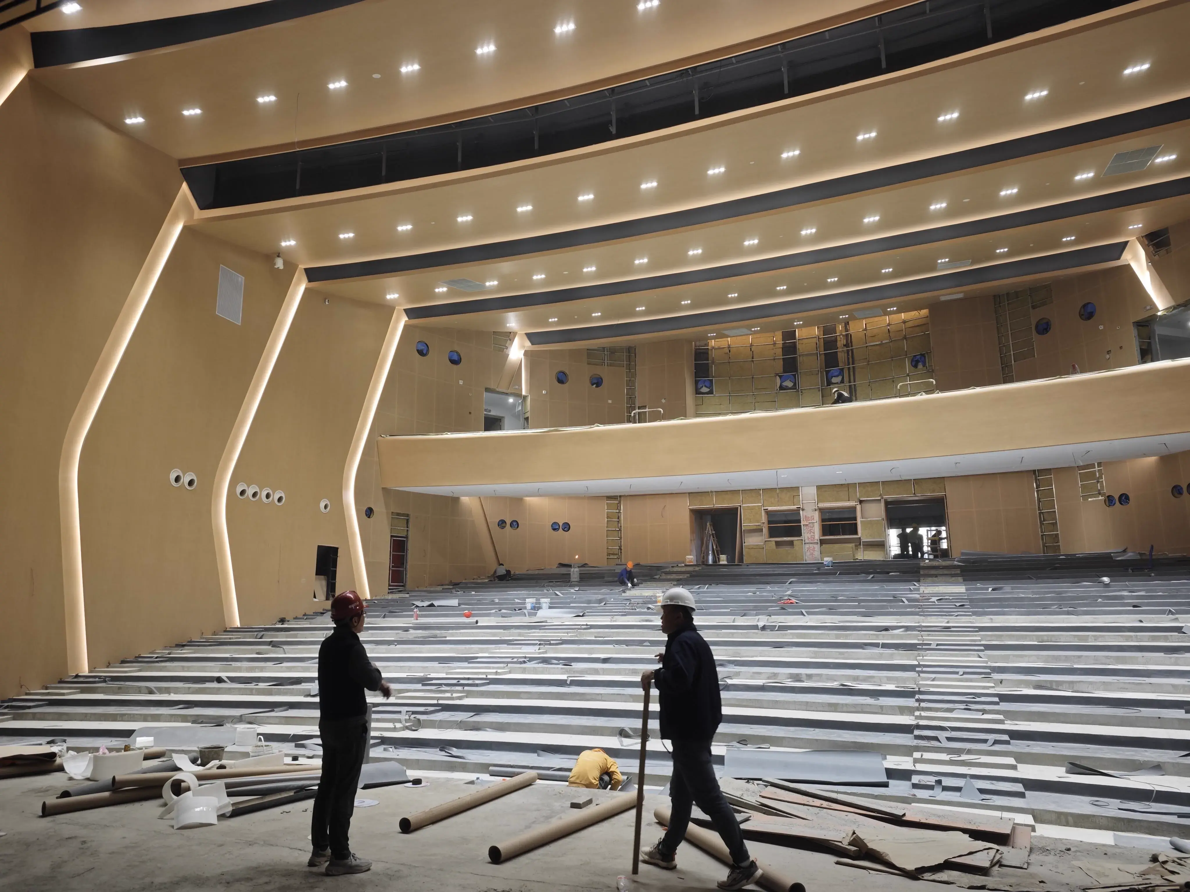 Auditorium construction phase with tiered seating base framework and workers in the audience area