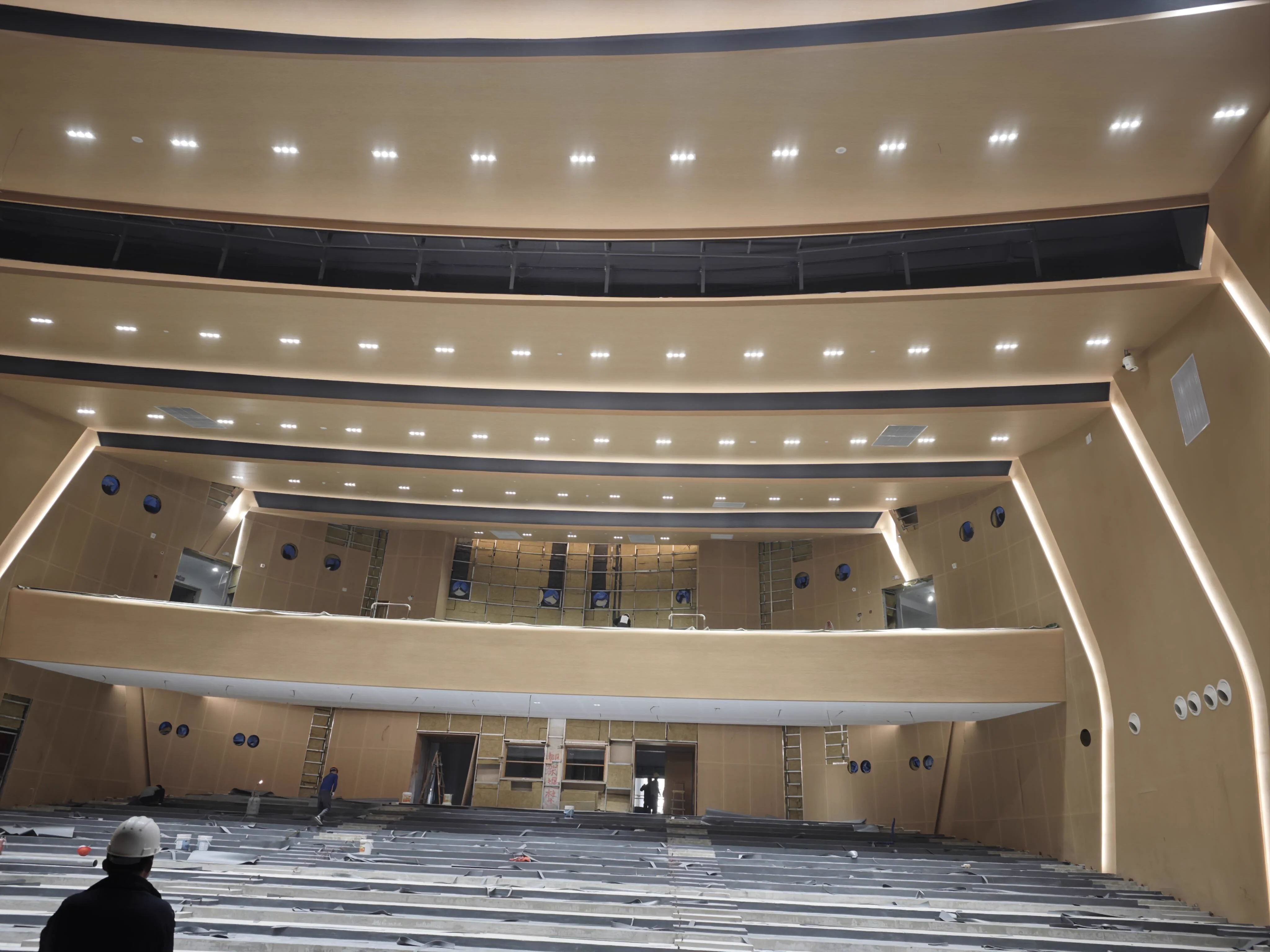 Auditorium construction phase showing balcony edge, ceiling lighting slots, and seating base