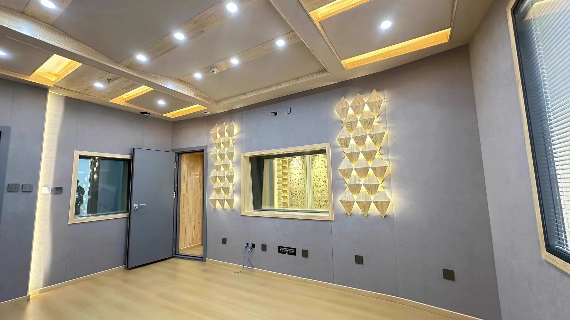 Recording room wall with acoustic observation windows and triangular backlit wooden diffusers